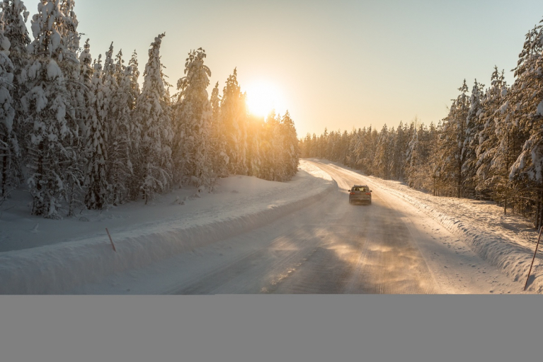 Auto talvisella tiellä auringonlaskussa