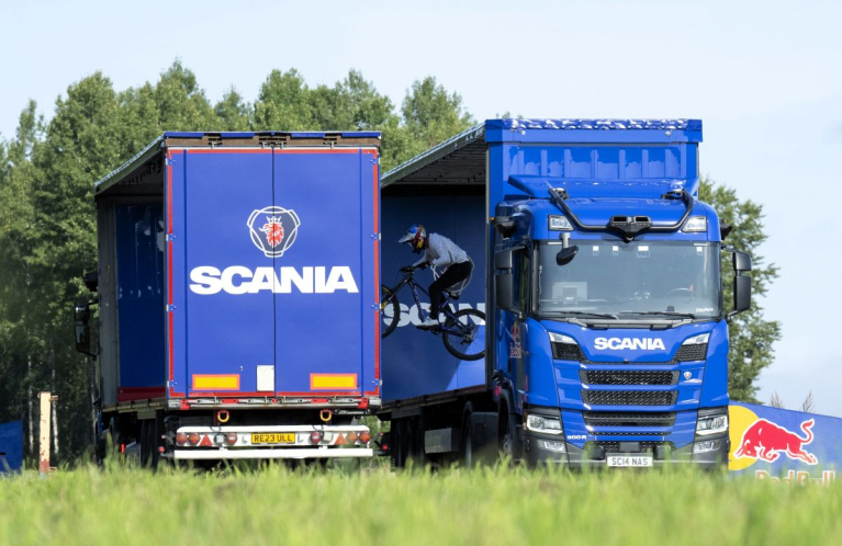 Two Scania autonomous trucks on a country road, going past each other in perfect sync to create a window of less than a second, allowing professional mountain biker and Red Bull Athlete Matt Jones to successfully jump between the two self-driving trucks.