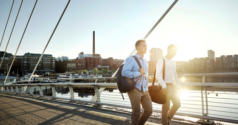 kaksi miestä kävelemässä sillalla, taustalla kaupunkimaisema