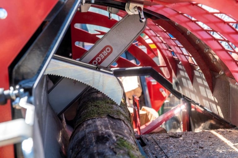 A close-up view of the interior of a large red forestry machine: several saws are positioned against a thin tree trunk for demonstration purposes.