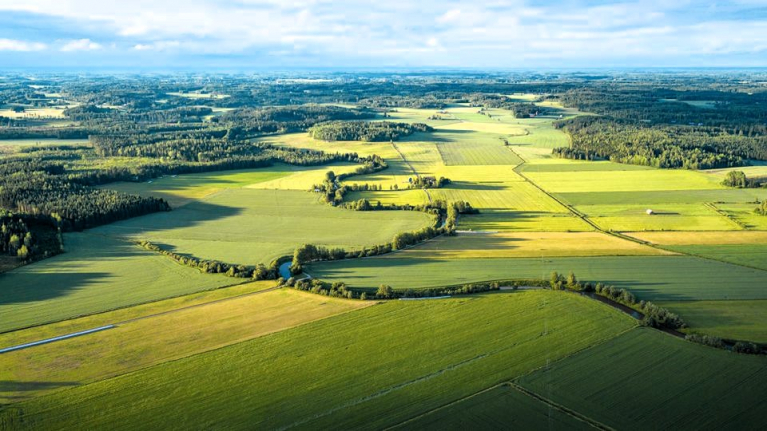 Ilmakuva suomalaisesta maa- ja metsätalousmaisemasta, jossa pellot ja metsäalueet vuorottelevat.