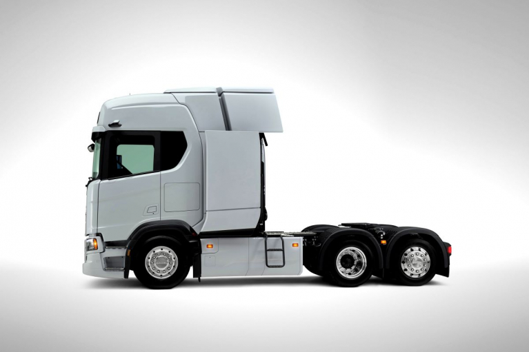 Side view of a white Scania electric tractor unit with three axles and an extended section behind the cab for additional batteries.