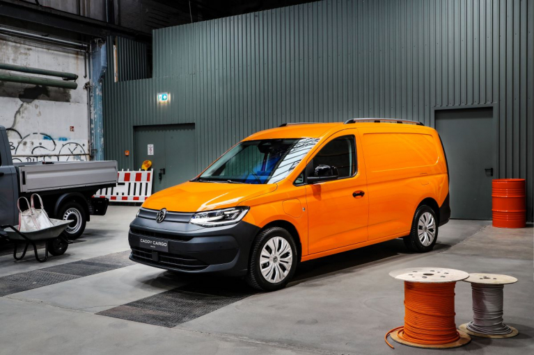 Oranssi Volkswagen Caddy Cargo Maxi -pakettiauto teollisuushallissa etuviistosta kuvattuna.