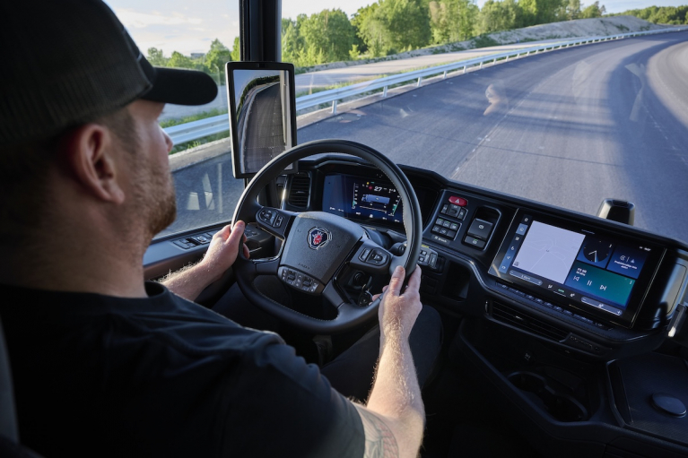 Scania Dynamic -kuorma-auton kuljettaja ohjaamossa, jossa näkyvät digitaalinen mittaristo, kamerapeilin näyttö ja keskusnäyttö.