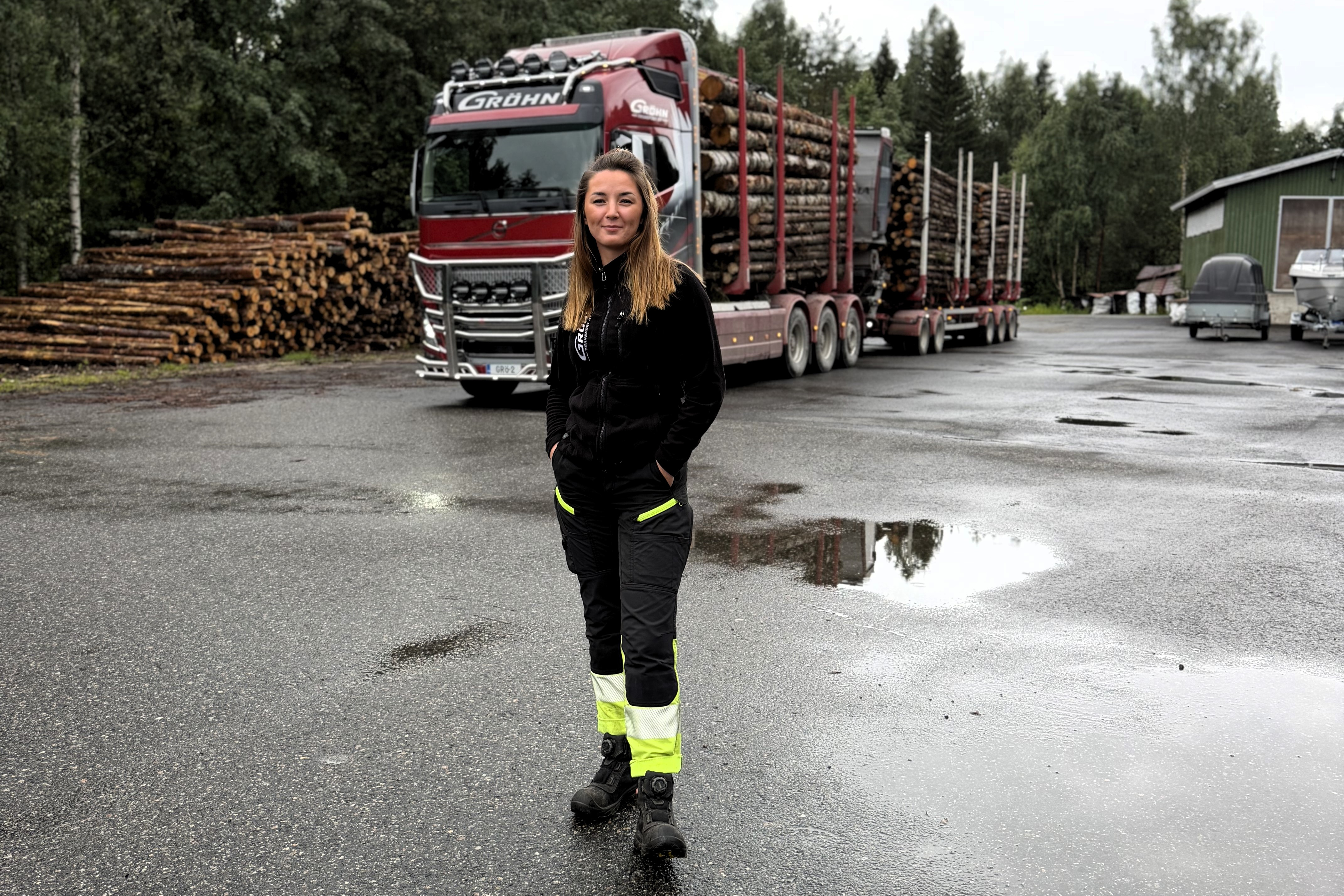 Marita Tiensuu seisoo pihalla Gröhn Transportin punaisen, puukuormassa olevan Volvo-puutavarayhdistelmän edessä.