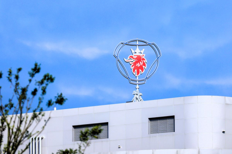 Scania’s griffin emblem above a white industrial building against a blue sky.