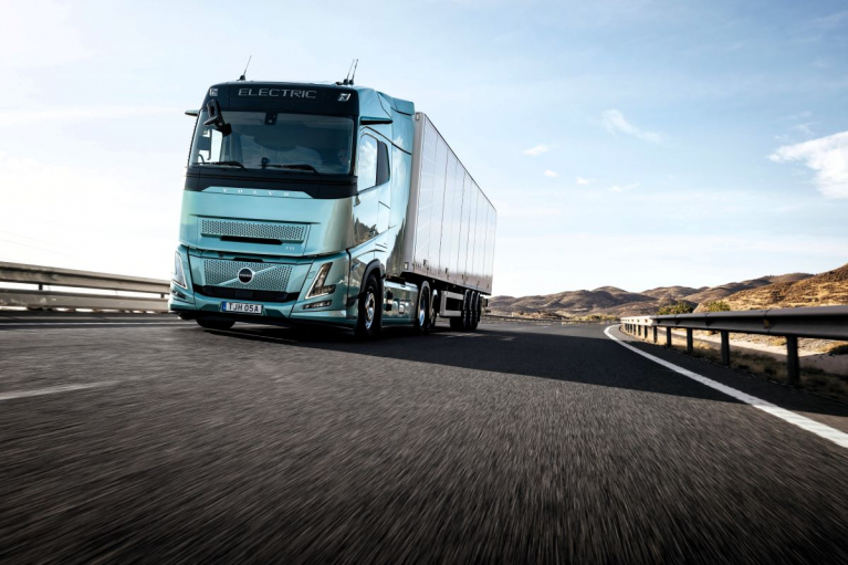 Vaaleanvihreä Volvo FH Aero Electric -sähkökuorma-auto vetää puoliperävaunua kaarteisella maantiellä.
