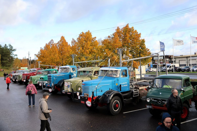 Vanhoja kuorma-autoja rivissä yleisön katseltavana. Etualalla on sininen puutavara-auto ja vihreä Mercedes-Benz Unimog.