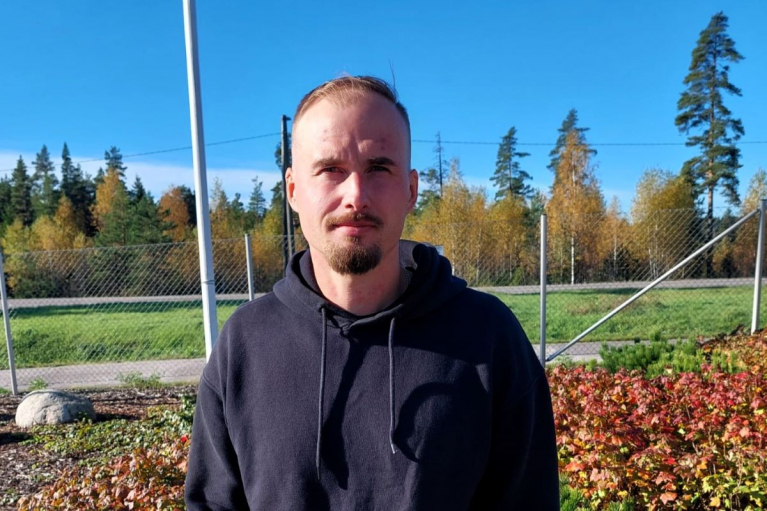 Metsäkoneenkuljettaja Henri Rämä seisoo ulkona mustassa hupparissa, taustallaan syksyisiä puita.