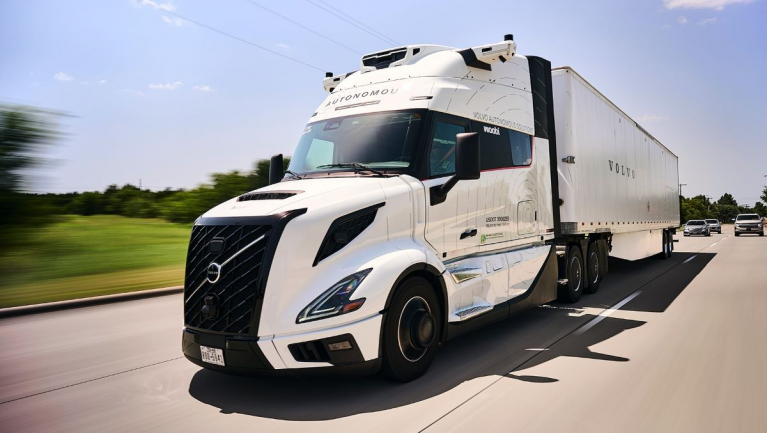 White Volvo VNL Autonomous truck with roof-mounted sensors hauling a box trailer on a highway.