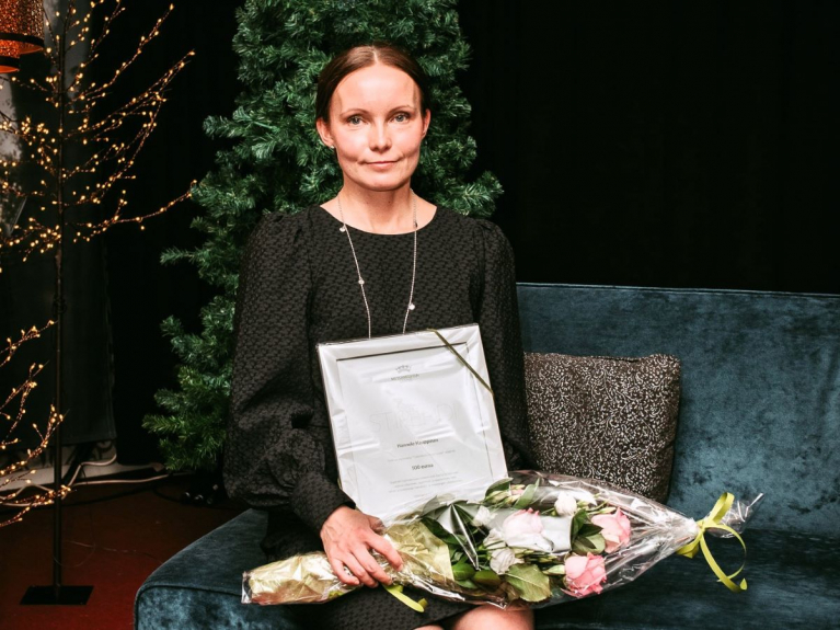 Hannele Kauppinen istuu sohvalla Metsämiesten Säätiön stipenditodistus ja kukkakimppu sylissään.