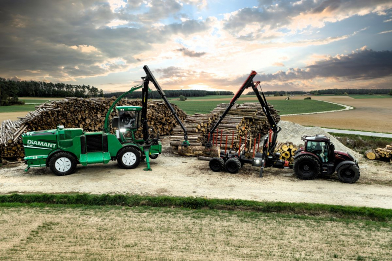 An ALBACH Diamant wood chipper and a tractor with a PIRK forestry trailer beside stacks of timber.