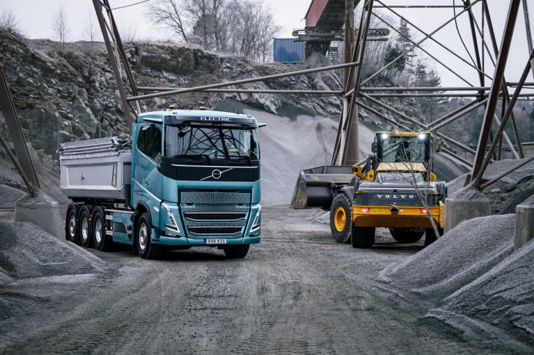 A Volvo FH Electric tipper truck and a Volvo wheel loader among aggregate stockpiles at a quarry.