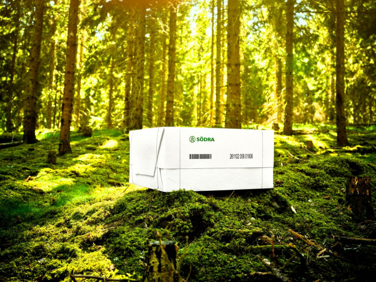 A white pulp bale bearing the Södra logo on a moss-covered forest floor, with sunlight filtering through the trees.