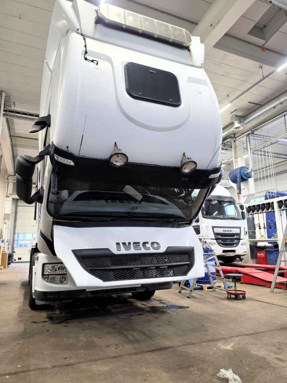 Valkoinen IVECO-kuorma-auto ohjaamo eteen kallistettuna Nordic Truckcenterin huoltohallissa. Taustalla on DAF-kuorma-auto.