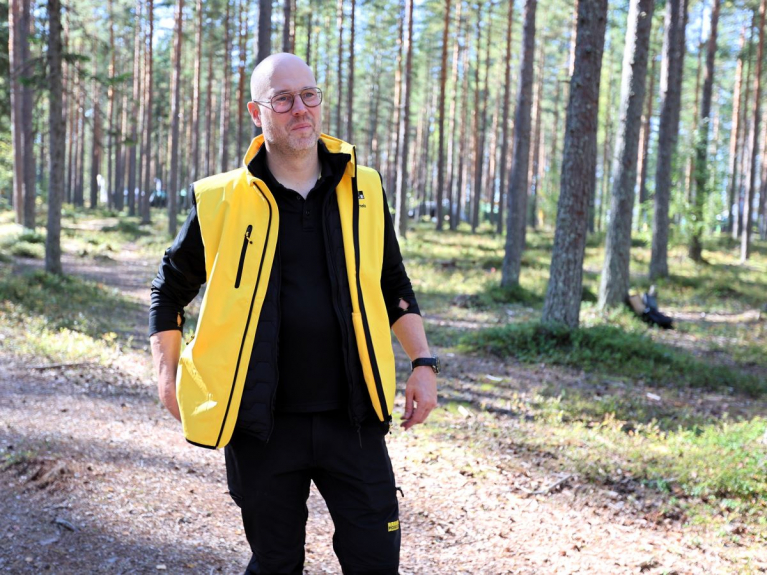 Ponsse President and CEO Juho Nummela standing in a pine forest wearing a yellow vest.