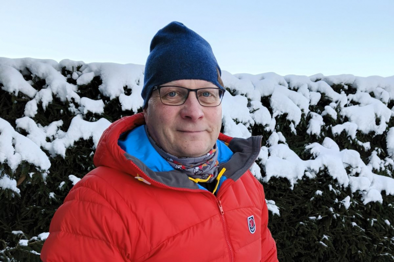 Meton puheenjohtaja Stefan Borgman punaisessa talvitakissa ja sinisessä pipossa lumisen pensasaidan edessä.