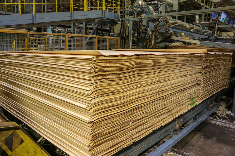 A large stack of thin wood veneer sheets on a plywood mill production line.